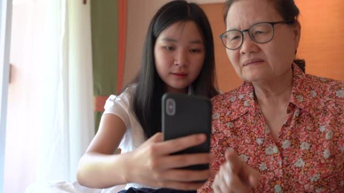 亚洲漂亮的侄女教她的祖母使用智能手机和新技术感到幸福和微笑，家庭观念