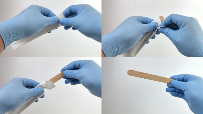 戴蓝色医用手套的医生打开一次性无菌医用刮刀。用于检查口腔和扁桃体的木制刮铲的宏观视频。