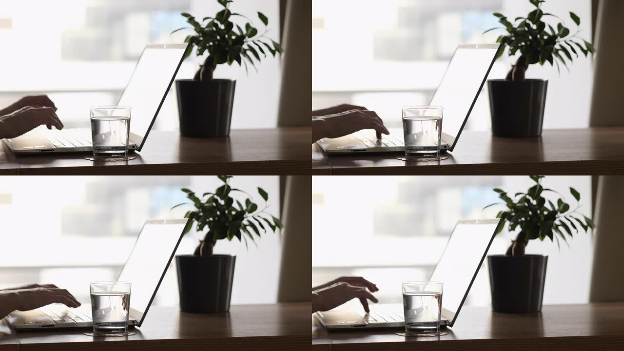 女性博客自由职业者在家庭办公室工作笔记本电脑。使用触摸板关闭女性的手。女人在窗户旁边的台式机上使用笔