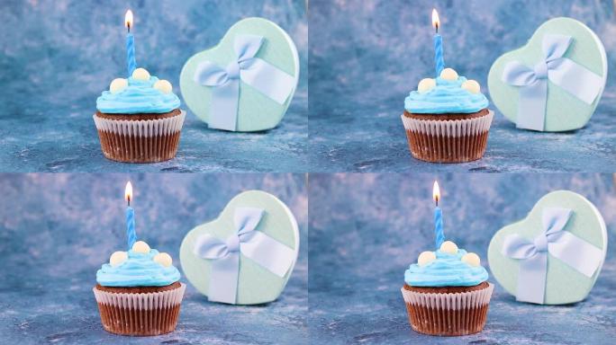 美味的巧克力杯蛋糕装饰着蓝色奶油，并出现在桌子上。杯蛋糕上燃烧的蓝色生日蜡烛