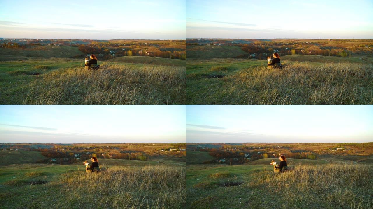 主人和宠物美国斯塔福德郡梗犬在日落时坐在绿山上
