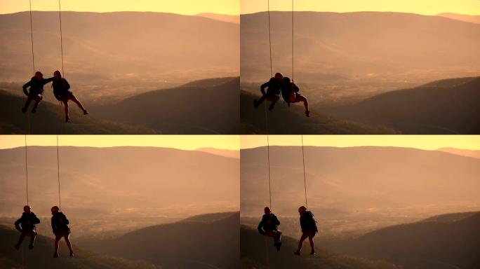 日落山顶上的攀绳队的夫妻。亲吻