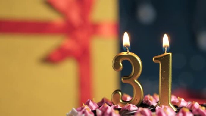生日蛋糕编号31点灯燃烧的金色蜡烛，蓝色背景礼物黄色盒子用红丝带绑起来。特写和慢动作