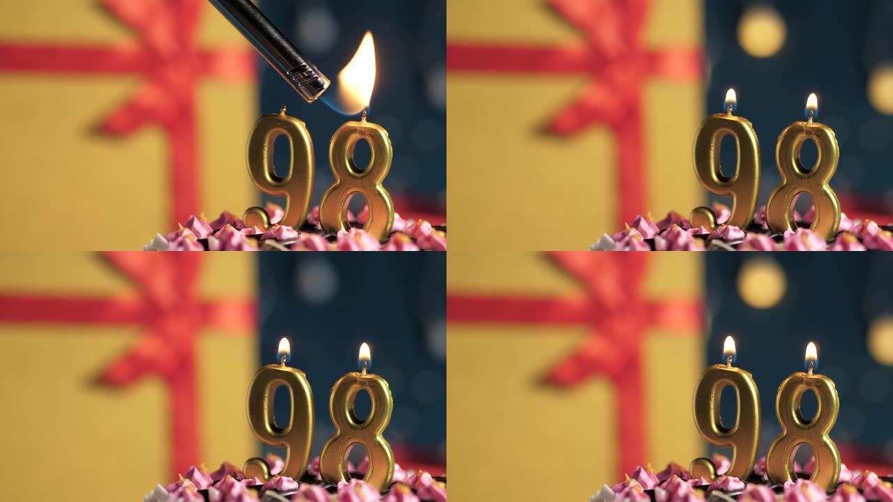 生日蛋糕98号点火器燃烧的金色蜡烛，蓝色背景礼物黄色盒子用红丝带绑起来。特写和慢动作