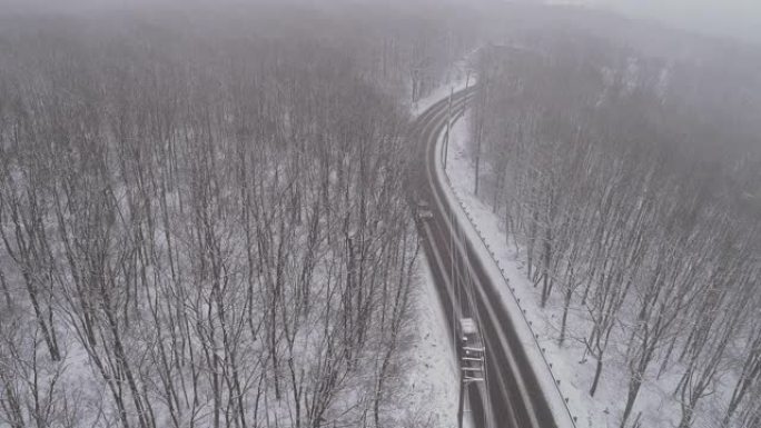 在降雪下驾驶高速公路穿过森林的汽车。带有静态摄像机的无人机航拍视频。
