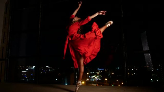一个穿着红色优雅连衣裙的女孩在一个带有夜城的大窗户的背景下跳舞。独自在家和恋爱
