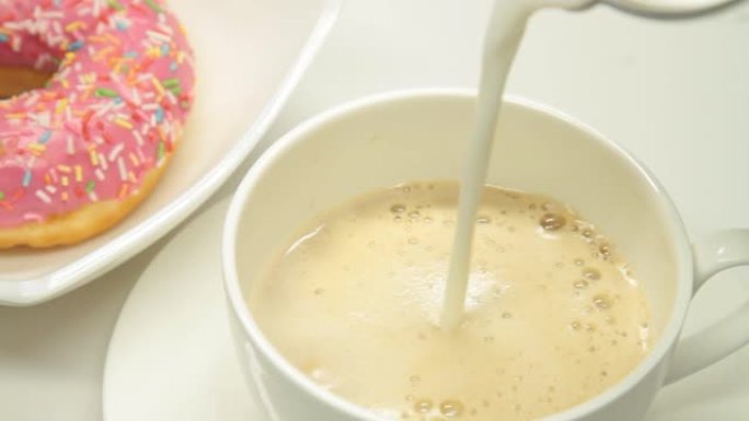 将牛奶倒入咖啡杯和草莓甜甜圈中