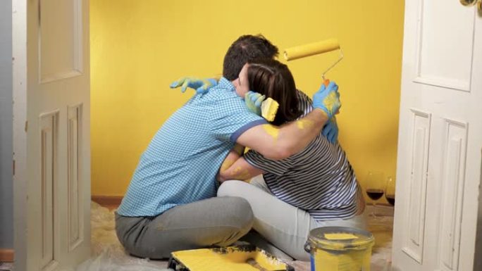 疲惫的男女夫妇坐在地板上。他们在情感上拥抱，并在工作结束时感到高兴。油漆修复工作超过了概念。慢动作