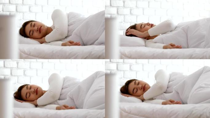 女人在舒适的白色卧室里用空气净化器睡觉，用于过滤和清洁去除家庭中的灰尘PM2.5 HEPA，用于新鲜