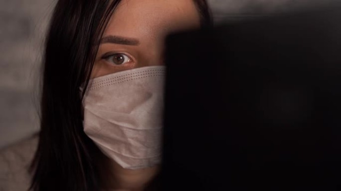 戴着医用口罩的妇女使用笔记本电脑从互联网上了解有关冠状病毒的新闻。女性担心自己的健康。冠状病毒的流行
