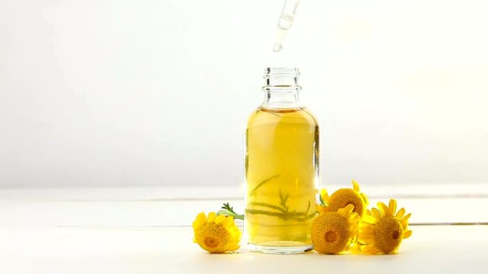 美丽的玻璃瓶中白色背景上的黄色Camomille花朵的精华