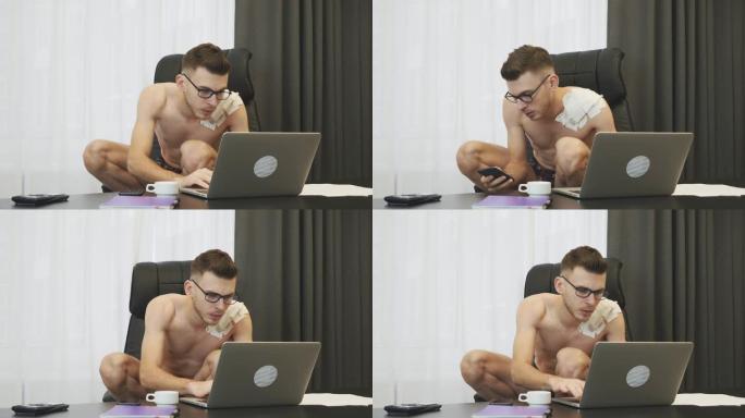 一个男人蹲在椅子上在办公室用笔记本电脑工作。穿着内衣在笔记本电脑上打字的男人。年轻的经纪人坐在自己的