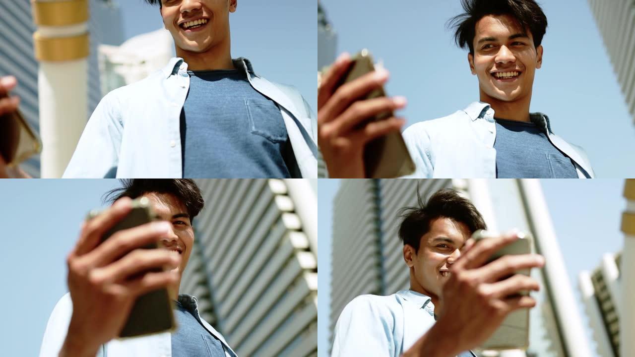 一个快乐的年轻人在城市使用手机。轨道射击。慢动作。以现代建筑为背景