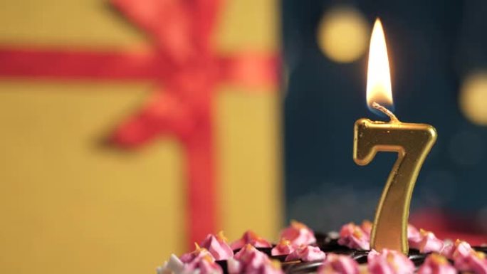 生日蛋糕7号点火器燃烧的金色蜡烛，蓝色背景礼物黄色盒子用红丝带绑起来。特写和慢动作