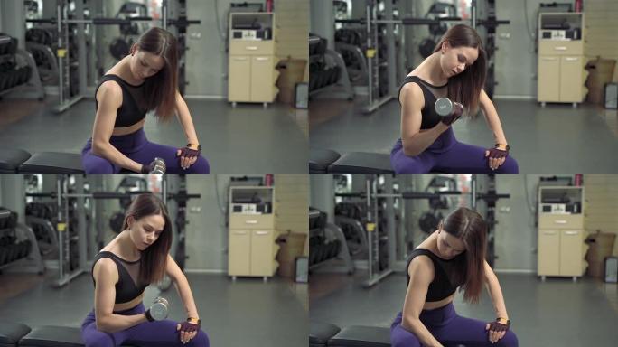 迷人的健身女孩在健身房用哑铃练习锻炼。年轻女子在体育俱乐部举重。