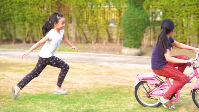 两个亚洲小女孩在花园里骑自行车