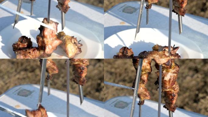 野餐时，用刀子将在烤架上油炸的新鲜开胃猪肉块从烤串中取出，放入开阔天空下的盘子中。高加索户外食物和烧