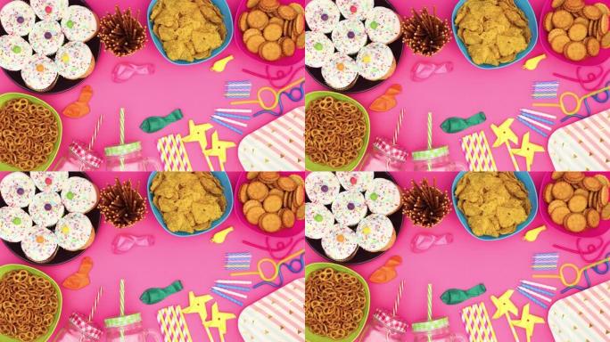 生日派对装饰品，杯蛋糕，食物，气球，吸管，蜡烛在粉红色背景上移动-停止运动