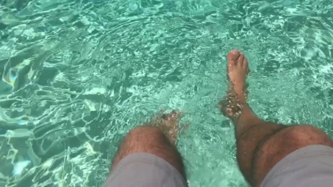 一个男人的腿在游泳池水中冷却的观点。