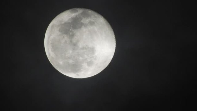 阴暗的夜晚满月。云彩从月亮掠过，实时拍摄。