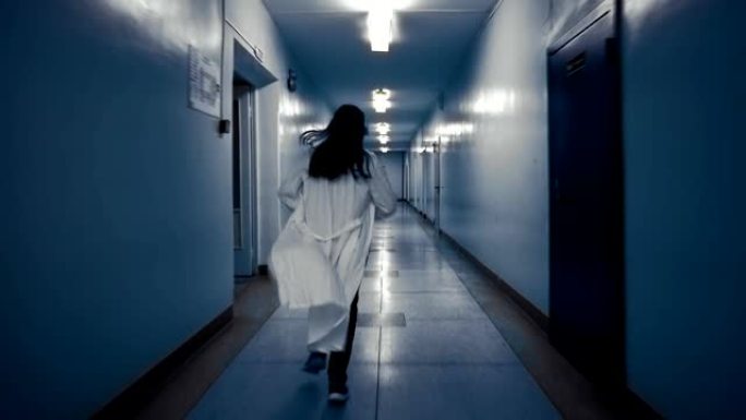穿着白大褂的女人在黑暗的走廊上奔跑，从后面看。