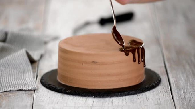 用融化的巧克力给巧克力蛋糕上釉。女人在蛋糕上倒巧克力。自制可可分层蛋糕。