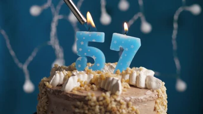 蓝色背景上有57号蜡烛的生日蛋糕。蜡烛着火了。慢动作和特写视图