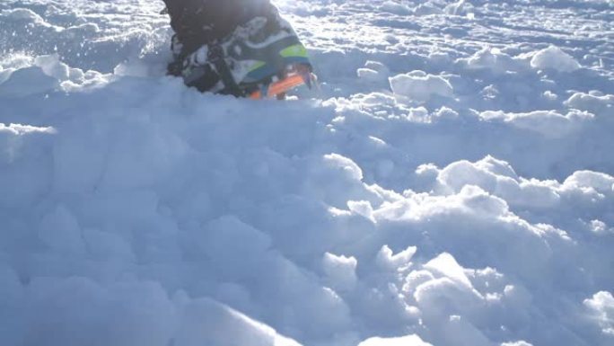 带有冰爪的山靴和带有背光太阳光束的雪地绑腿的特写镜头。高高的登山者在坚硬的雪中猛击靴子，登上山顶。