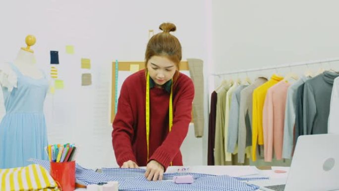 亚洲女性时装设计师在亚洲小型企业家庭工作室的办公桌上使用面料