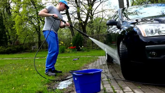 男性工人在露天用电动喷水洗车。