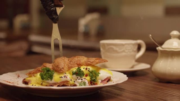 将羊角面包中的蛋汁倒入盘子中的慢动作。专业厨师用叉子切成羊角面包煎蛋卷。餐厅内餐桌上的早餐。在红色史