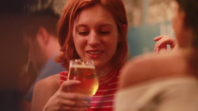 坦率的年轻红发女人晚上喝啤酒和朋友说话