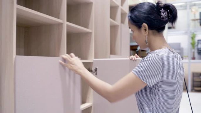 亚洲女性顾客购物和选择餐桌和书籍货架木材作为家庭装饰。亚洲女性在购物商店购买五金和家具。