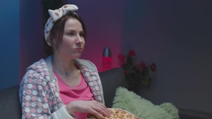 女人在电视上看搞笑电影，在沙发上吃爆米花