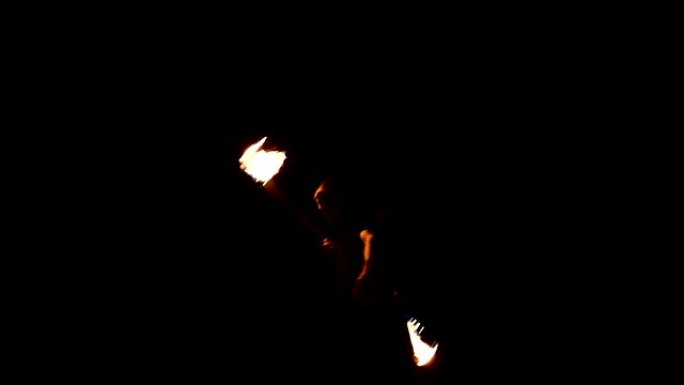 消防表演。男人用两把燃烧的火把玩杂耍。夜场。掌握法克尔。低角度