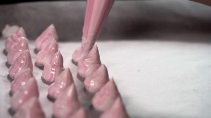 烤盘上管道蛋白酥皮混合物的特写视图。自制粉红色蛋白酥皮之吻，从管道袋中压出混合物