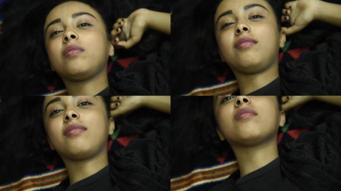 美丽微笑的中东少女穿着黑色上衣，在卧室里放松。一名年轻的中东妇女小睡后的肖像白天在家床上睡觉，情绪积