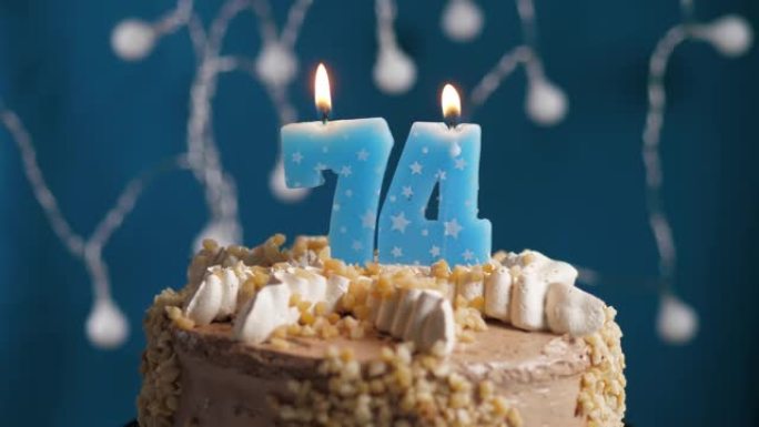 蓝色背景上有74号蜡烛的生日蛋糕。蜡烛吹灭了。慢动作和特写视图