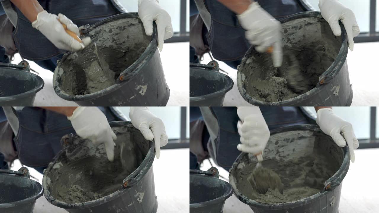 4k关闭高级杂工手使用抹刀在桶中搅拌混凝土水泥砂浆，用于准备家庭装修维修施工或瓷砖铺路。高级杂工di
