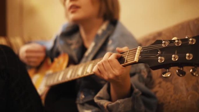 女孩弹吉他，在沙发上唱歌。女人在室内创作音乐。艺术家在bas吉他上表演。音乐家创作旋律。一个少年正在