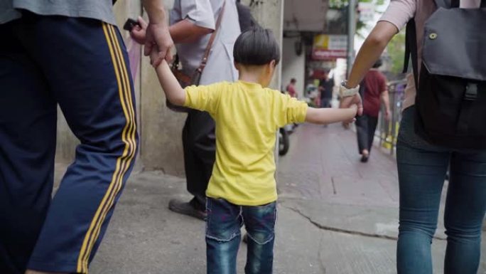 一个小男孩与家人一起旅行并在泰国曼谷的城市街道上行走的慢动作镜头