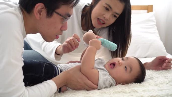年轻的亚洲父亲家庭与妻子温柔地亲吻他的男婴。男人和女人享受与孩子在一起的时光