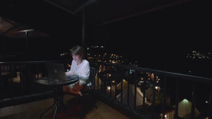 穿着浴袍的女人晚上在酒店套房使用笔记本电脑