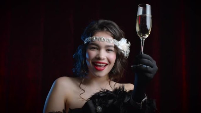 穿着盖茨比风格的复古风格的女人举起一杯香槟，像吐司一样，在丝绒背景上喝葡萄酒。咆哮的二十年代，复古，