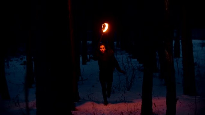 年轻女子带着火炬在夜晚的冬季森林中奔跑