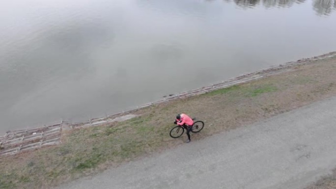 站在大湖附近的公路自行车专业自行车手。铁人三项运动员准备进行自行车训练的俯视图。戴着头盔和骑行服的女