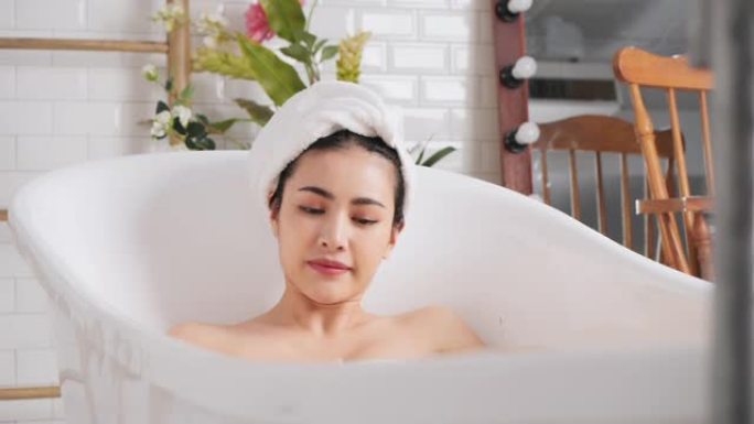 慢动作: 亚洲女性在浴缸里沐浴在她的身体和腿上。