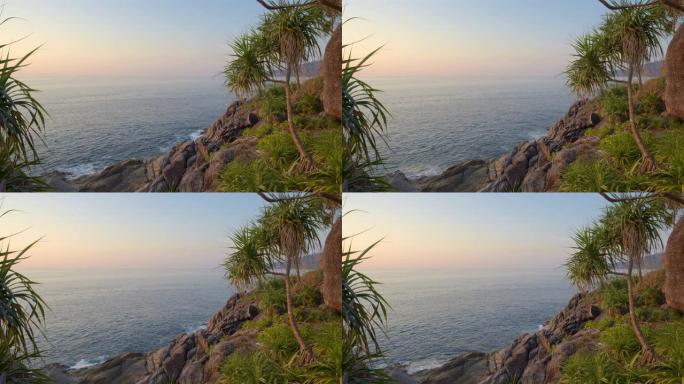 在温暖的日落期间，从岩石海滩上的山丘上可以看到大海