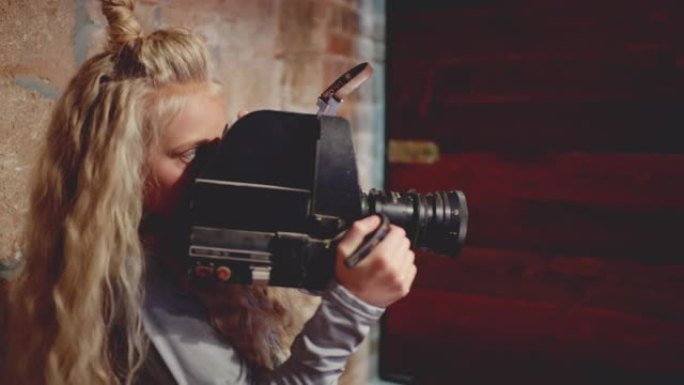 年轻女孩摄影师在布里克工作室用复古相机拍摄视频。女孩视频操作员在砖背景的艺术工作室用老式相机拍摄电影