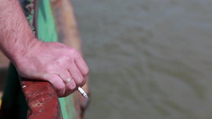 男性手在桥上或船上抽烟。在河流的背景上。